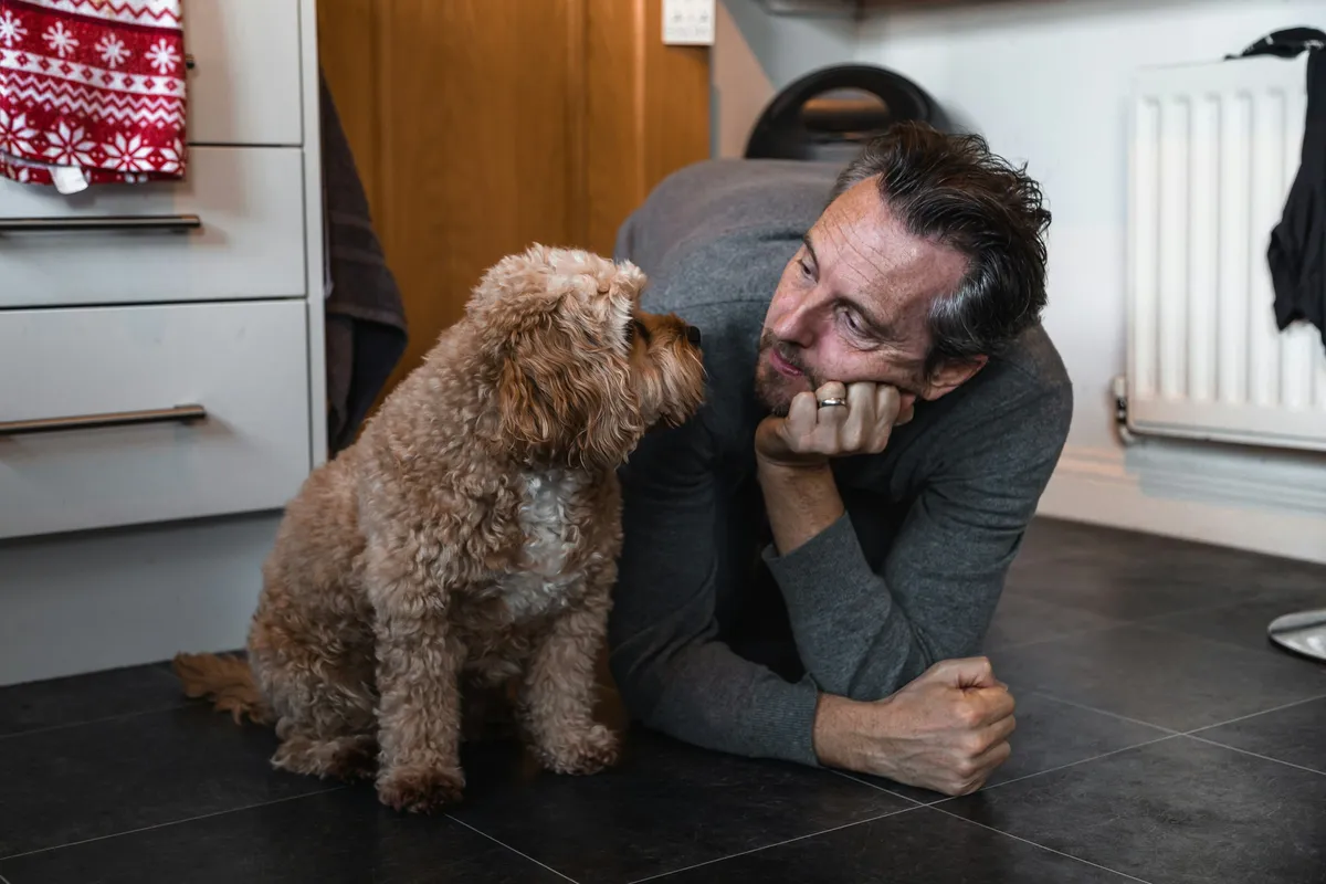 A man in a dark sweater holding a small long-haired brown dog close to his chest
